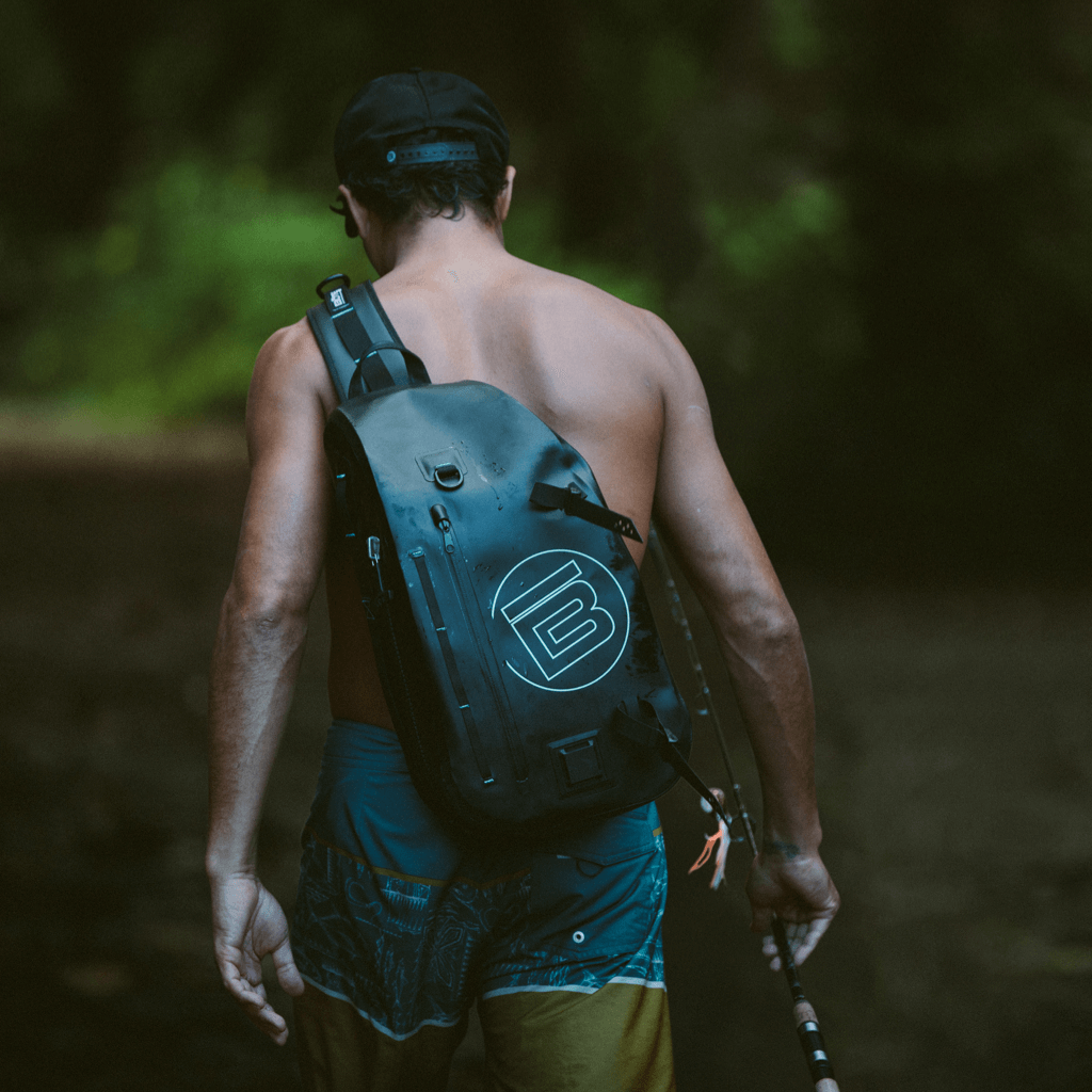 Man carrying his fishing rods in hand with the black Highwater Slingpack on his back