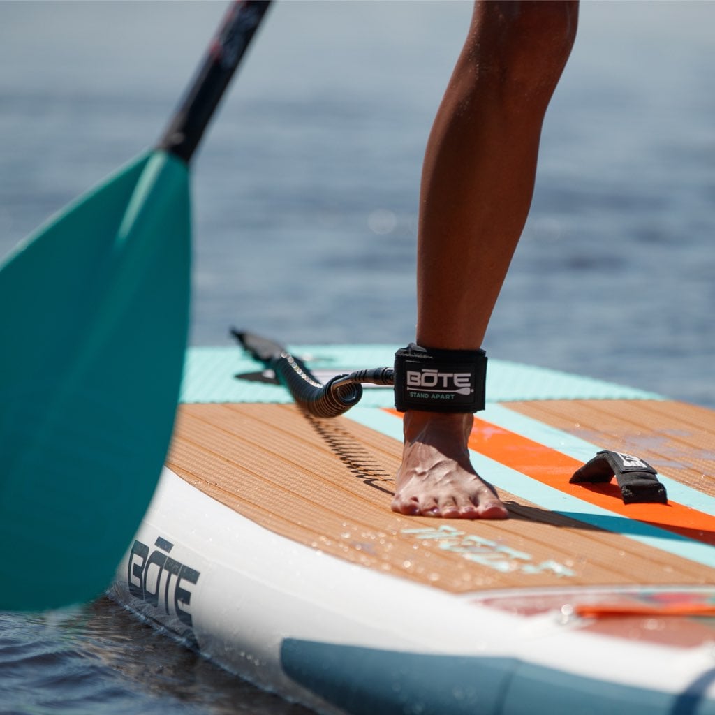 BOTE coiled leash in use, attached to paddle board and wrapped around paddler’s ankle.
