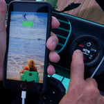 Hand pressing Power Rac control panel button next to charging phone on paddle board.