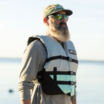 Man wearing the BOTE Adult Universal Foam PFD Vest while standing near the water in outdoor sunlight.