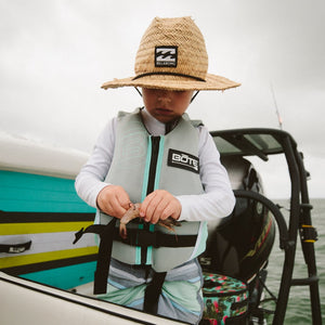 Child on a boat wearing the BOTE Child Foam PFD Vest while baiting a fishing hook.